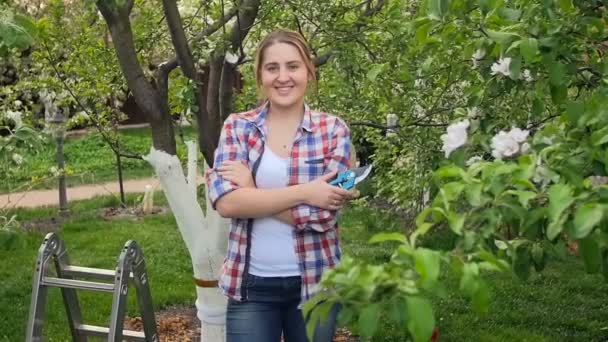 Zeitlupenaufnahme einer jungen Frau, die mit Gartengeräten im Obstgarten posiert — Stockvideo