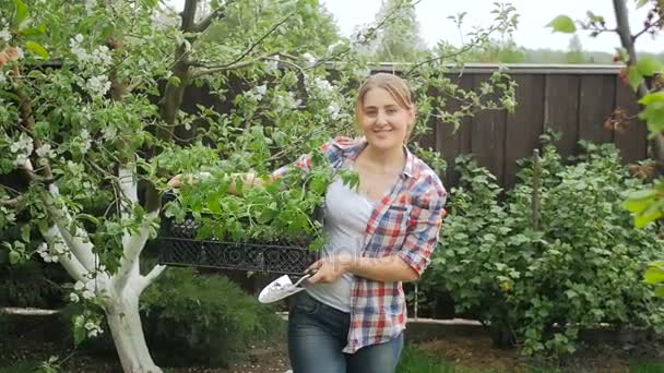 Hermosa mujer sonriente caminando con plántulas en caja en el jardín — Vídeo de stock