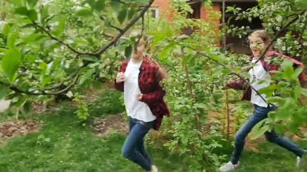 Медленное видео двух счастливых девочек, играющих в контакт и бегающих в саду — стоковое видео