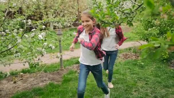 Lento tiro movimento de meninas alegres felizes jogando e correndo no jardim sob macieiras — Vídeo de Stock