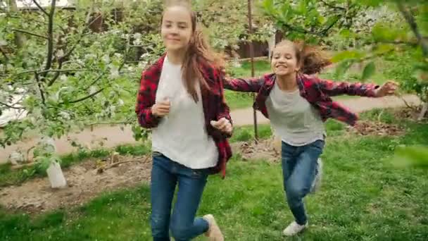 Медленная съемка двух счастливых девушек, бегающих и играющих в мяч в саду — стоковое видео