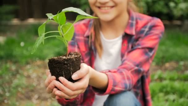 Vídeo em câmera lenta de menina sorridente bonito segurando mudas de plantas no jardim / Conceito de nova vida — Vídeo de Stock