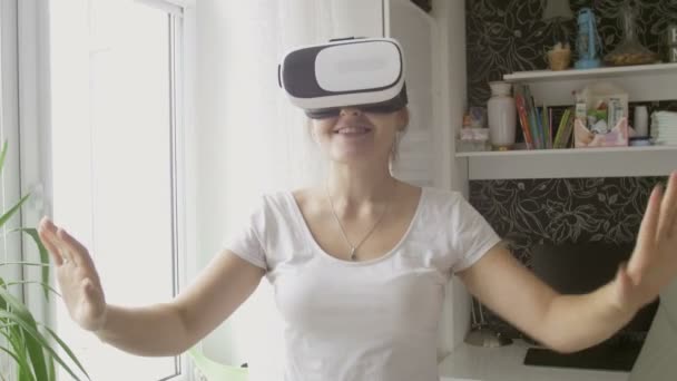 Giovane donna sorridente che indossa auricolare realtà virtuale a piedi a casa. Filmato girato a 4K — Video Stock