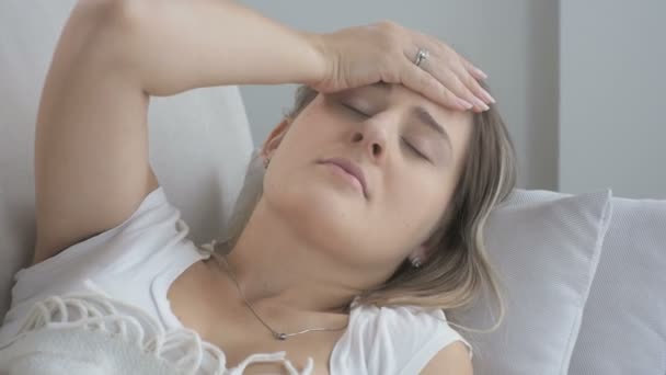 Vértes fiatal nő szenved fejfájás feküdt a kanapé a nappaliban. 4 k felbontású felvételeket a lövés — Stock videók