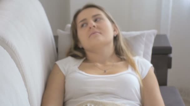 Крупный план молодой больной женщины, сидящей на диване в гостиной и чихающей бумажной салфеткой. Съемка в 4K — стоковое видео