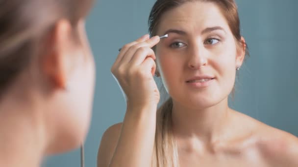 Imágenes 4K de la joven hermosa mujer arrancando las cejas en el espejo en el baño — Vídeos de Stock