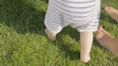 Çimüzerinde anne ile ilk adımları yaparken bebeğin ayakları üzerinde closeup atış