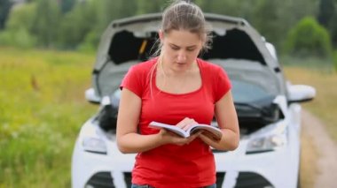 Genç kadın Brokedown arabaya ayakta ve manul ıssız kırsal yolda okuma okuma