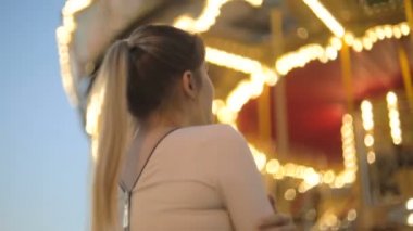 Fuarda ayakta ve ışıklı carousel seyir içinde güzel genç kadın