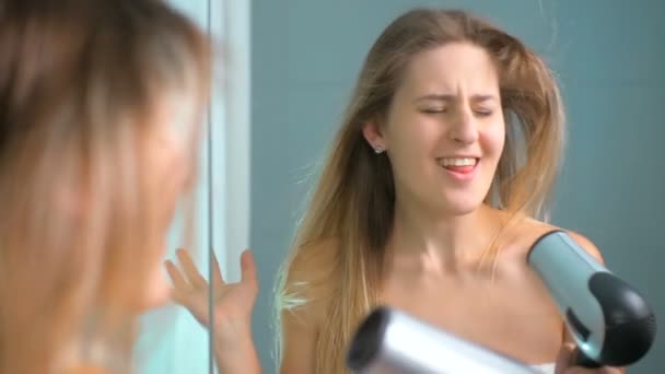 Медленная съемка красивой молодой женщины, поющей во время сушки волос — стоковое видео