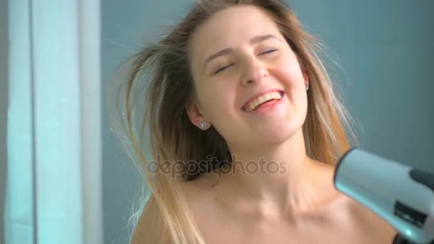 Медленная съемка счастливой улыбающейся женщины, сушащей волосы в ванной — стоковое видео
