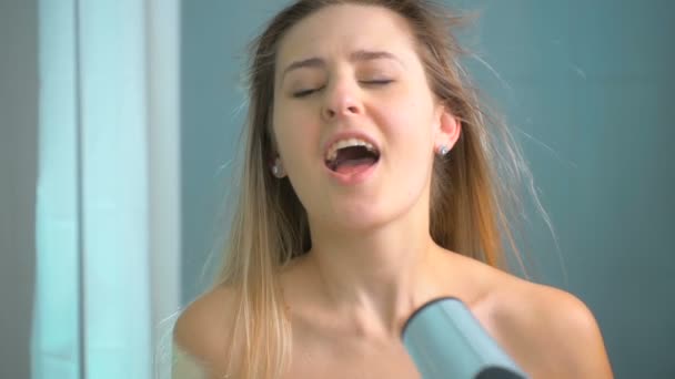Filmagem em câmera lenta da bela jovem mulher cantando no secador de cabelo no banheiro — Vídeo de Stock