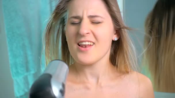 Медленная съемка красивой молодой женщины, поющей фен в ванной комнате — стоковое видео