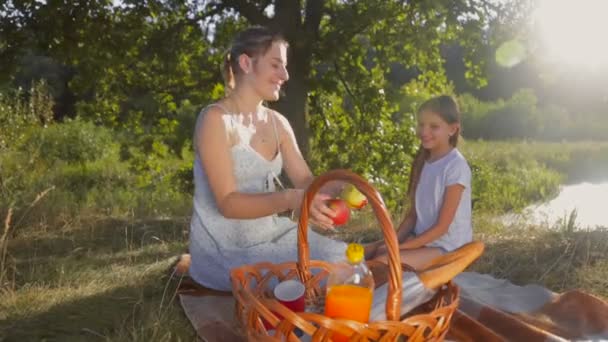 Счастливая улыбающаяся мать дарит яблоко своей дочери на пикнике в парке — стоковое видео