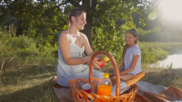 Glücklich lächelnde Mutter schenkt ihrer Tochter beim Picknick im Park einen Apfel — Stockvideo