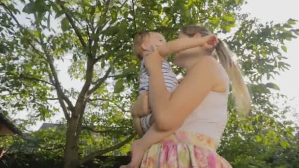 Retrato de jovem mãe abraçando seu bebê na sombra da árvore — Vídeo de Stock