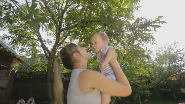 Glückliche junge Mutter hält ihren kleinen Sohn hoch oben im Obstgarten — Stockvideo