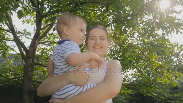 Glücklich lächelnde Mutter umarmt ihren kleinen Sohn unter Baum im Park — Stockvideo