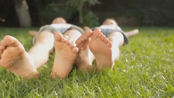 Dolly shot de deux filles pieds couchés sur l'herbe à chaud jour d'été — Video