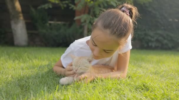 Портрет милої дівчини-підлітка з червоним кошеням на траві в саду — стокове відео