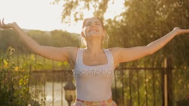 Porträt einer fröhlich lachenden Frau, die bei Sonnenuntergang Wasserspritzer aus Gartenschläuchen genießt — Stockvideo