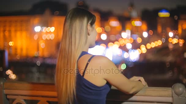 Hermosa mujer joven mirando paisaje urbano iluminado por la noche desde la azotea — Vídeos de Stock