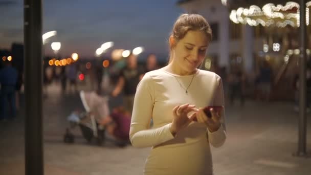 Kopfschuss einer schönen jungen Frau mit Smartphone auf belebter Straße in der Nacht — Stockvideo