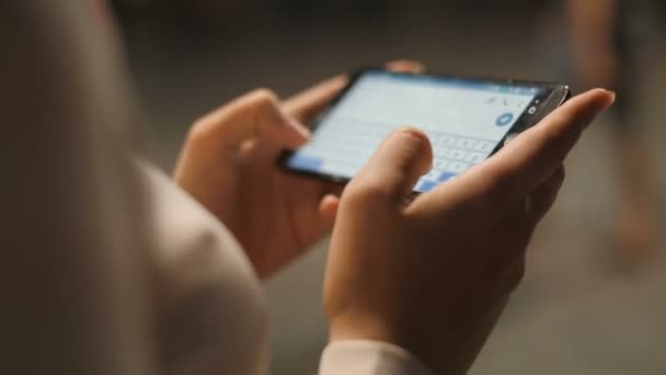 Closeup tiro de bela jovem mulher mensagens de texto no smartphone na rua à noite — Vídeo de Stock