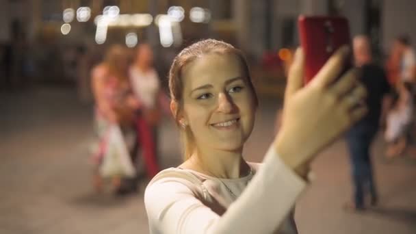 Mulher sorridente bonita fazendo tiro selfie no smartphone na rua da noite — Vídeo de Stock