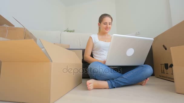 Dolly-Aufnahme einer glücklichen jungen Frau, die in ein neues Haus zieht und ein digitales Tablet benutzt — Stockvideo