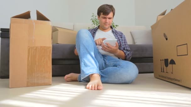 Dolly shot of young man using digital tablet while moving into a new house — Stock Video