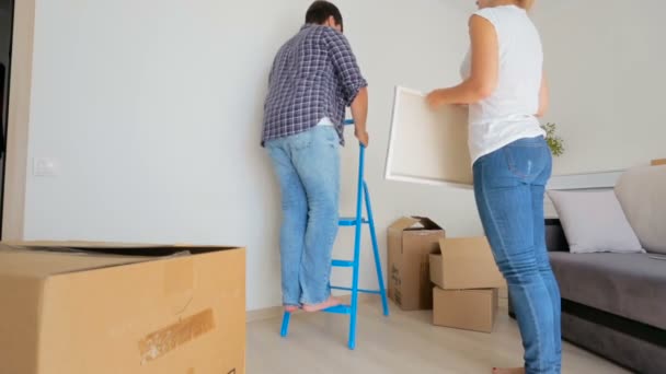 Pareja joven colgando pintura en la pared de su nuevo apartamento — Vídeos de Stock