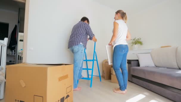 Gelukkige jonge paar kiezen plek voor schilderij op de muur van hun nieuwe appartement — Stockvideo