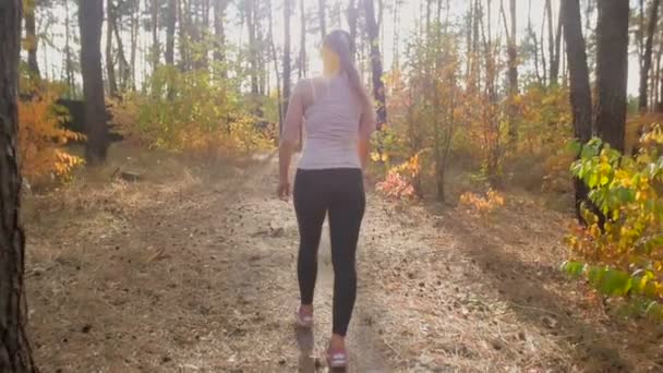 Lenta toma de la mujer joven en ropa deportiva caminando en el bosque de otoño — Vídeos de Stock