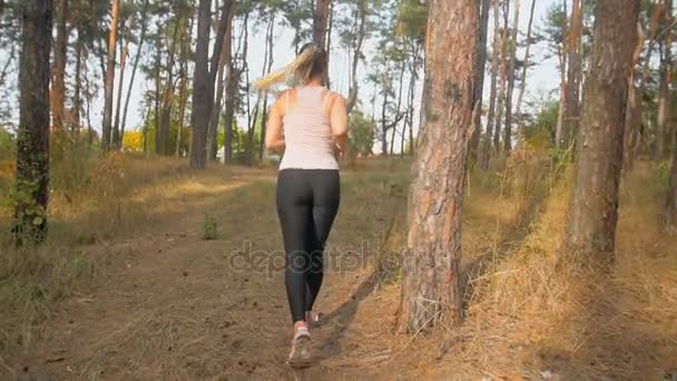 Bageste udsigt slow motion optagelser af aktiv ung kvinde kører op ad bakken i skoven om morgenen – Stock-video