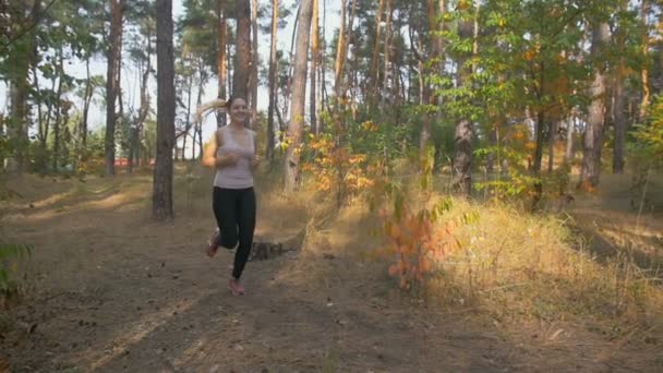 Movimiento lento de la joven sonriente corriendo por el sendero del bosque por la mañana — Vídeos de Stock