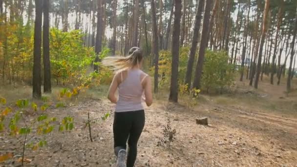 Vista trasera de cámara lenta de la joven corriendo rápido en el bosque — Vídeo de stock