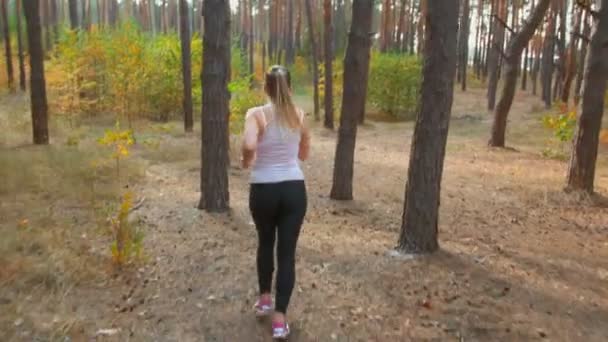 Imágenes de 4K de una mujer delgada y sexy corriendo en el bosque de otoño al atardecer — Vídeo de stock