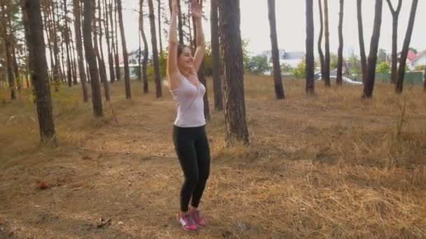 Zeitlupe einer jungen lächelnden Frau, die im Wald springt und trainiert — Stockvideo