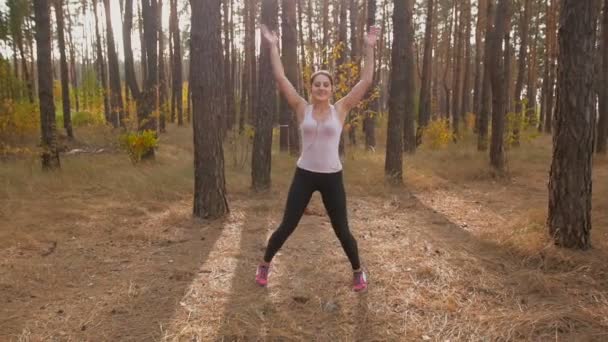 Lento movimento dolly tiro de bela mulher sorridente aquecendo antes de correr na floresta — Vídeo de Stock