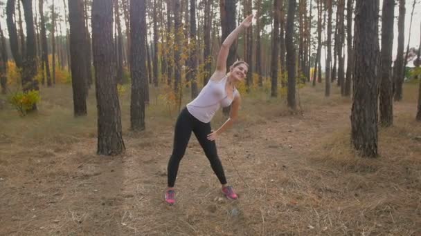 Imágenes en cámara lenta de mujeres jóvenes estirando el cuerpo antes de entrenar en el bosque — Vídeos de Stock