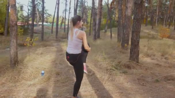 Imágenes 4K mujer joven estirándose y calentándose antes de trotar en el bosque — Vídeos de Stock