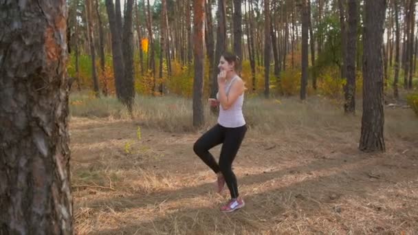 Dolly tiro de bela mulher sorridente se exercitando antes de correr na floresta — Vídeo de Stock