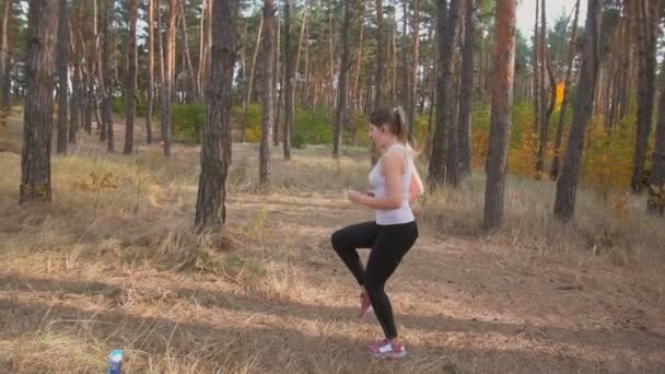 Imágenes en cámara lenta de una joven delgada calentándose en el bosque antes de correr — Vídeos de Stock