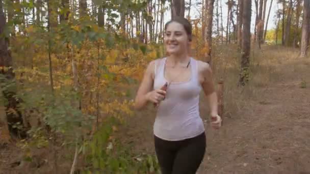 4k Filmmaterial der schönen jungen Frau, die mit Kopfhörern Musik hört, während sie im Wald joggt — Stockvideo