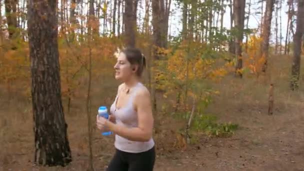 Steadicam tiro de bela jovem mulher bebendo água durante jogging na floresta — Vídeo de Stock