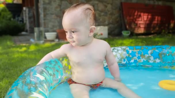 Feliz menino sorridente sentado na piscina inflável no jardim — Vídeo de Stock