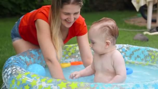 Boldog, mosolygós kisfiú játszó anya felfújható medence a kertben — Stock videók