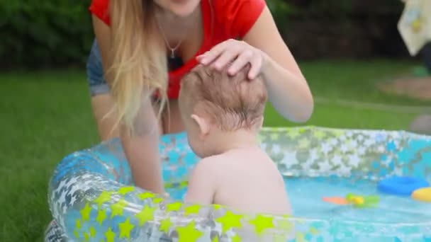 팽창 식 수영장에서 그녀의 1 년 오래 된 아들을 노는 행복 한 젊은 어머니 — 비디오