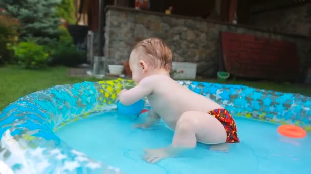 1 jaar oude peuter jongen spelen met in het opblaasbaar zwembad in tuin — Stockvideo